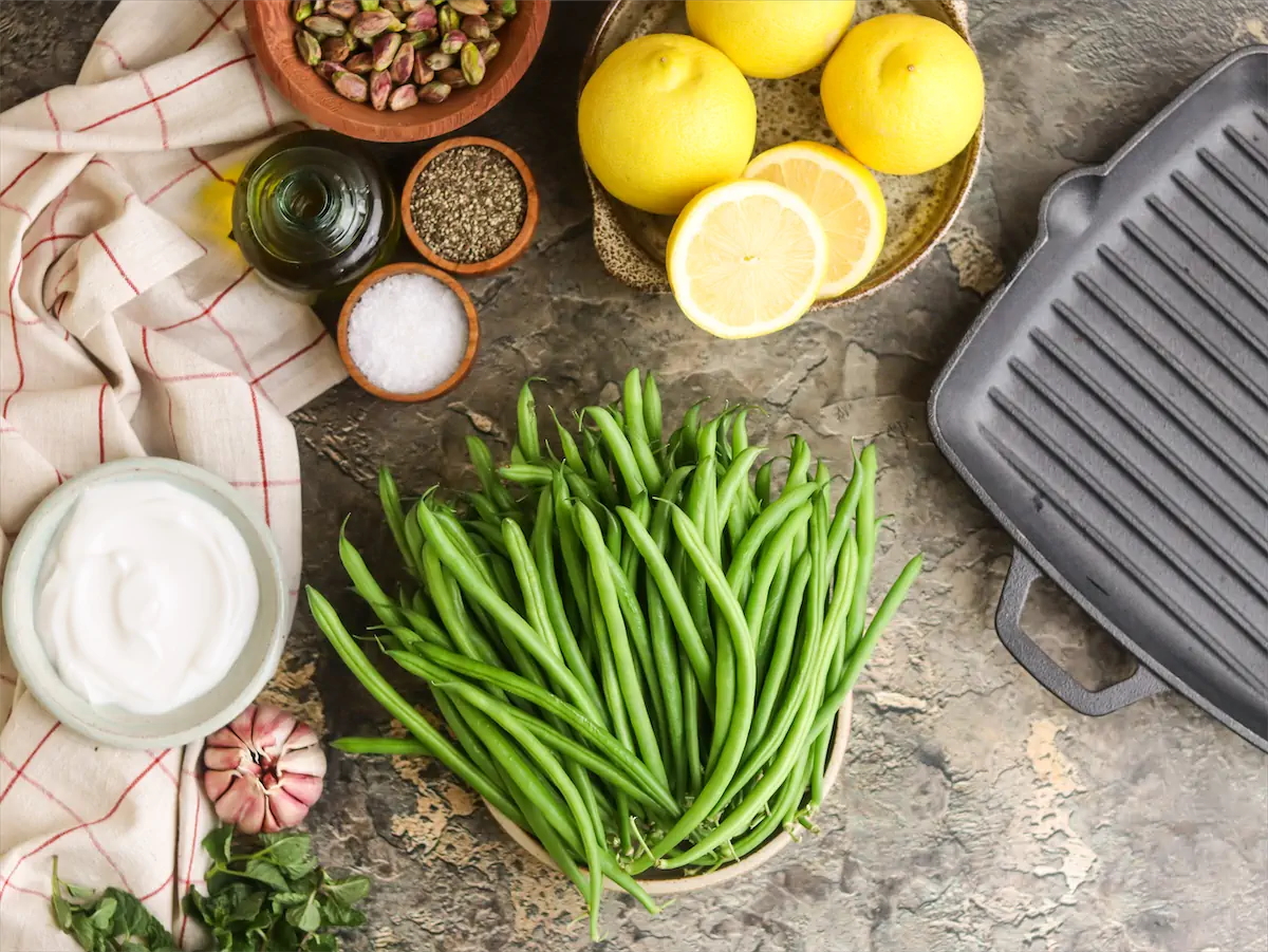 Green beans, de-shelled pistachio nuts, Greek yogurt, lemon and other ingredients arranged and displayed on the table to make grilled green bean salad.