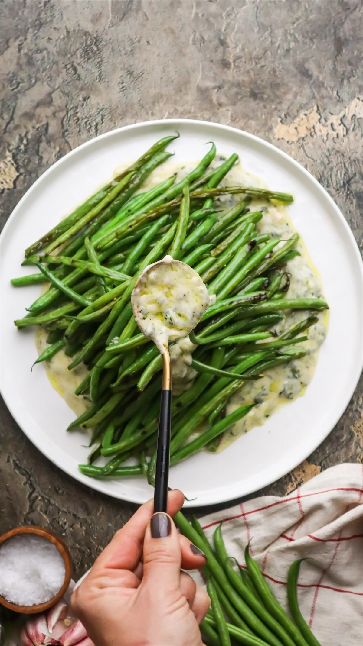 Drizzling yogurt and mint dressing with a spoon over a plate of grilled green beans.
