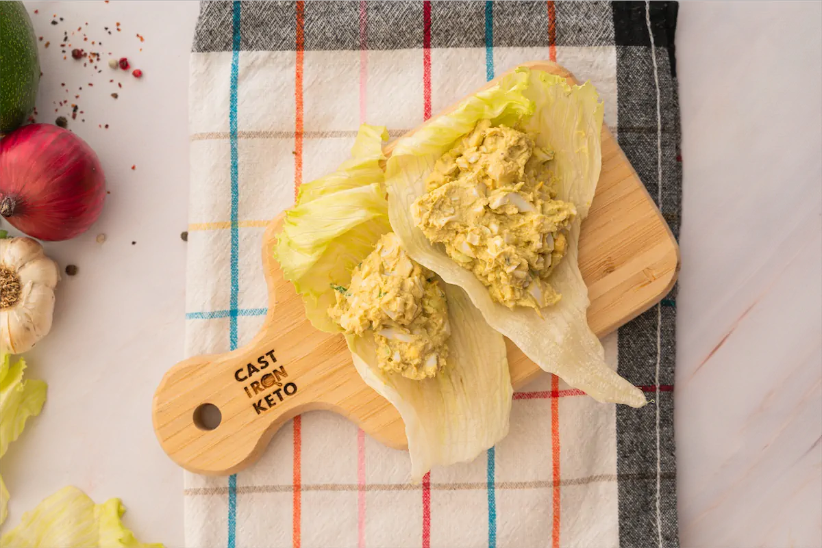 Avocado egg salad, served on a bed of lettuce leaves, served on a wooden board.