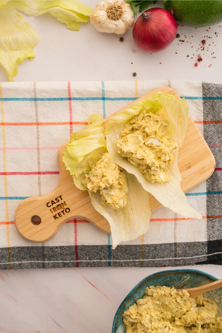 Egg avocado salad served on lettuce leaves and presented on a wooden board.