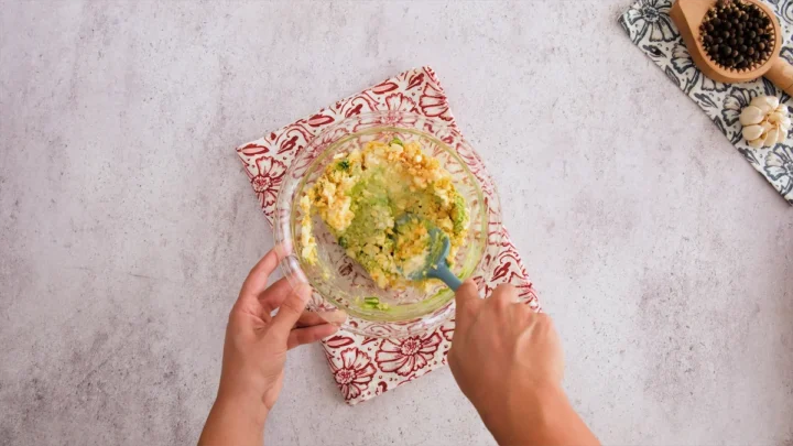 The necessary ingredients for making this homemade egg avocado salad are being mixed with a silicon spatula.