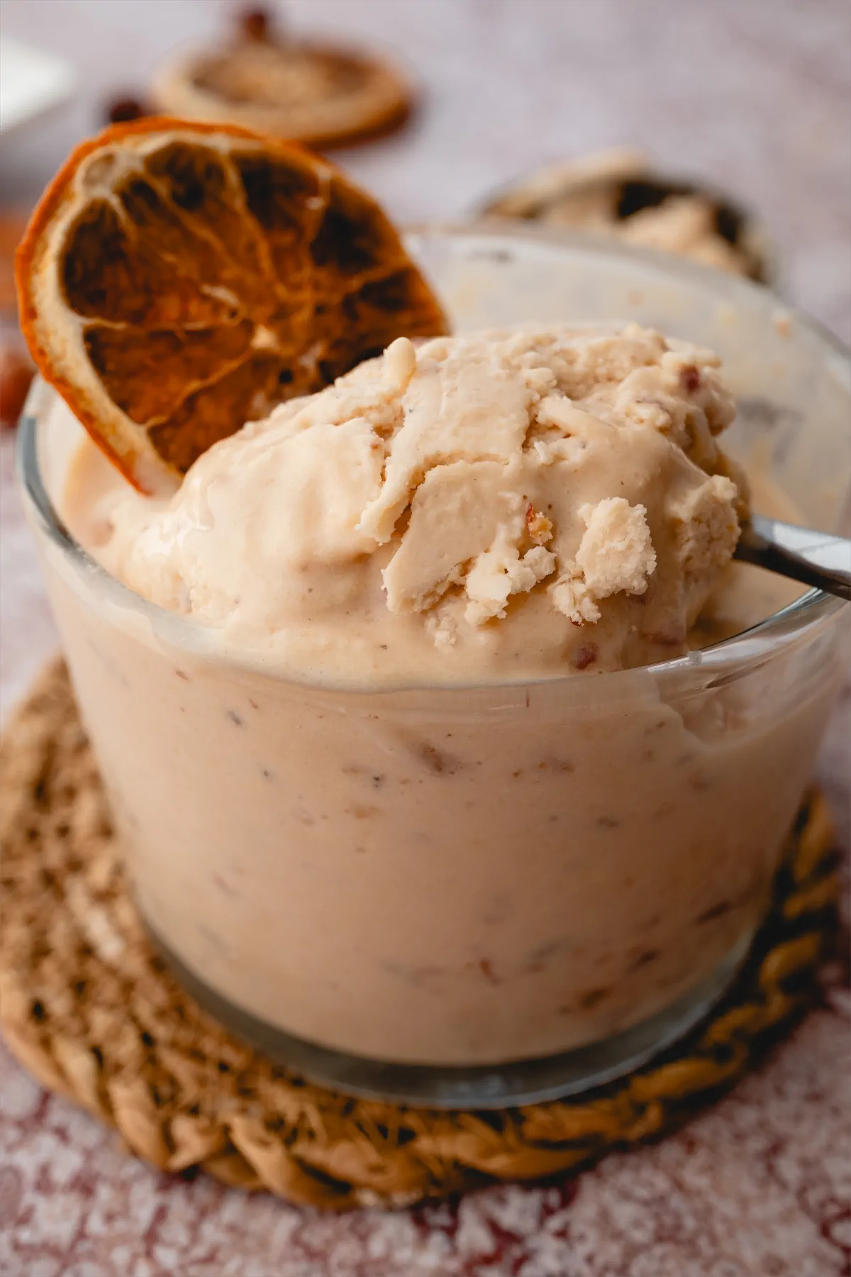 Keto butter pecan ice cream served with a slice of dried orange in a transparent glass container.
