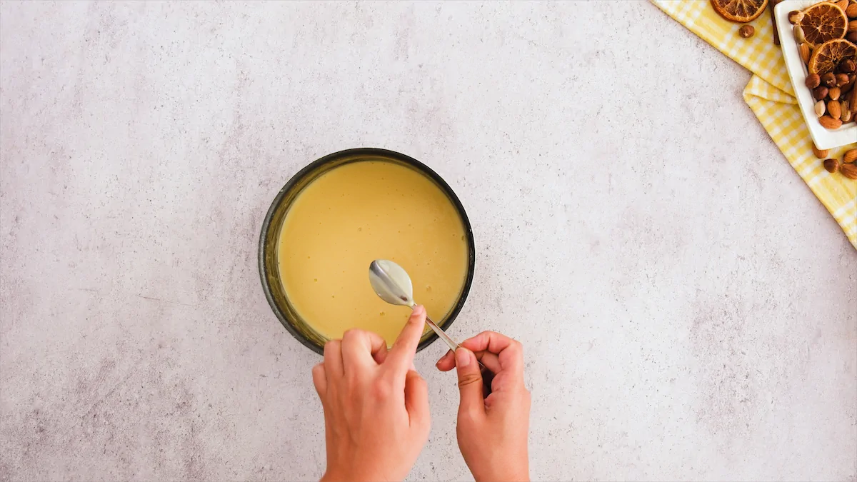 Two hands are using a spoon to check the custard's consistency.