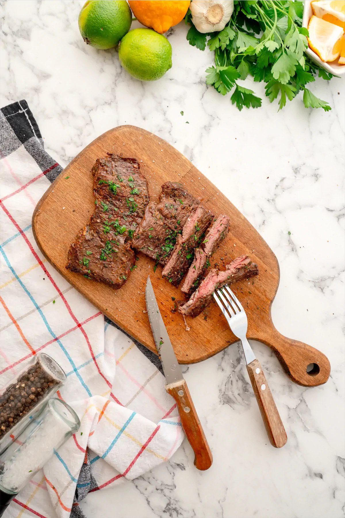 Two steaks are on a chopping board, and one of the keto carne asada is sliced using a fork and knife.