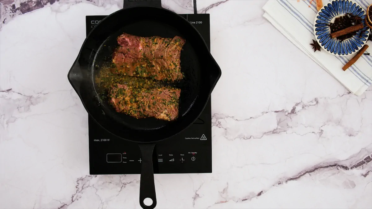 The steaks are getting cooked in a cast iron skillet on an induction stovetop.