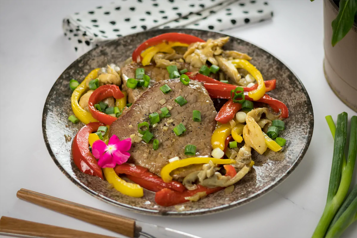 Homemade pork steaks with mushrooms and bell peppers, plated and garnished with green herbs."