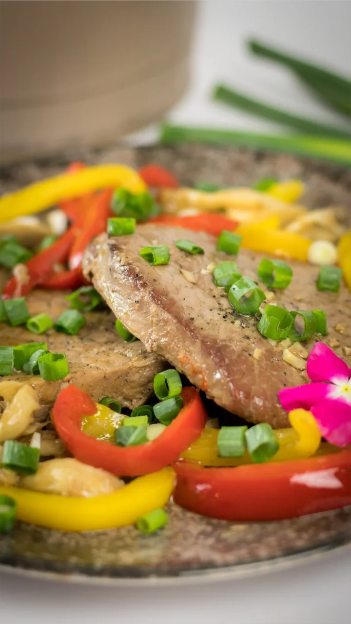 Homemade keto pork steak with mushrooms and red and yellow bell peppers served on a plate.