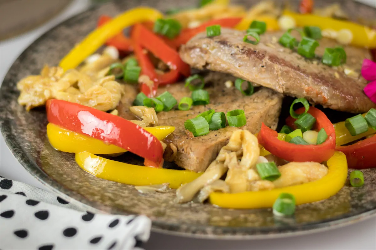 Keto pork steak with mushrooms, red and yellow bell peppers served on a plate, garnished with fresh herbs.