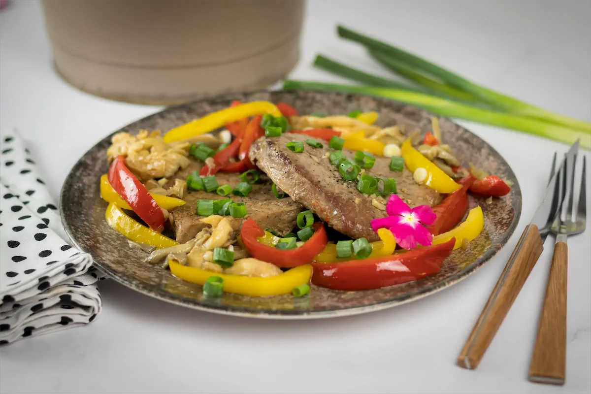 Keto pork steak with oyster mushrooms and red and yellow bell peppers served on a plate.