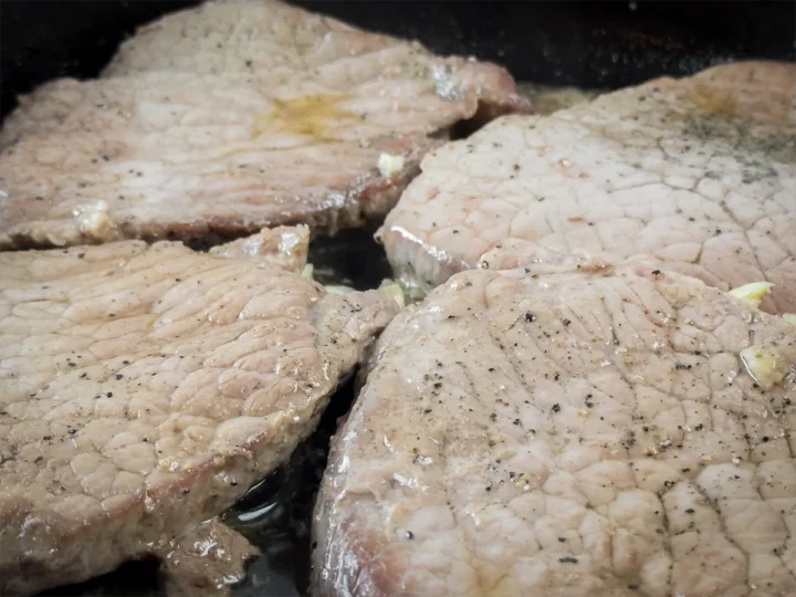 The pork steaks are cooking in a cast iron skillet with minced garlic.