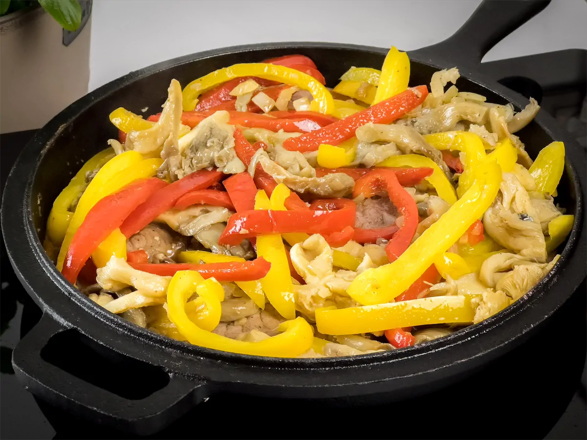 Bell peppers, mushrooms, and onions cooking in a cast iron skillet.