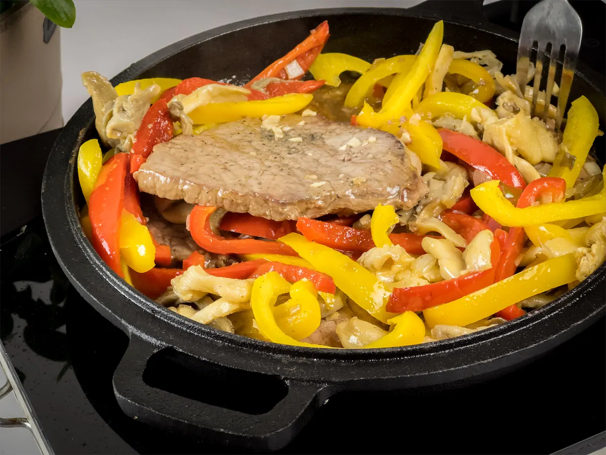 Keto pork steak on a cast iron skillet with red and yellow bell peppers.