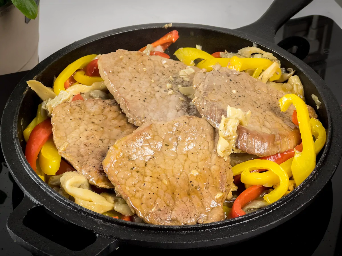 Pork steaks, mushrooms and bell peppers in a cast iron skillet ready to be served.