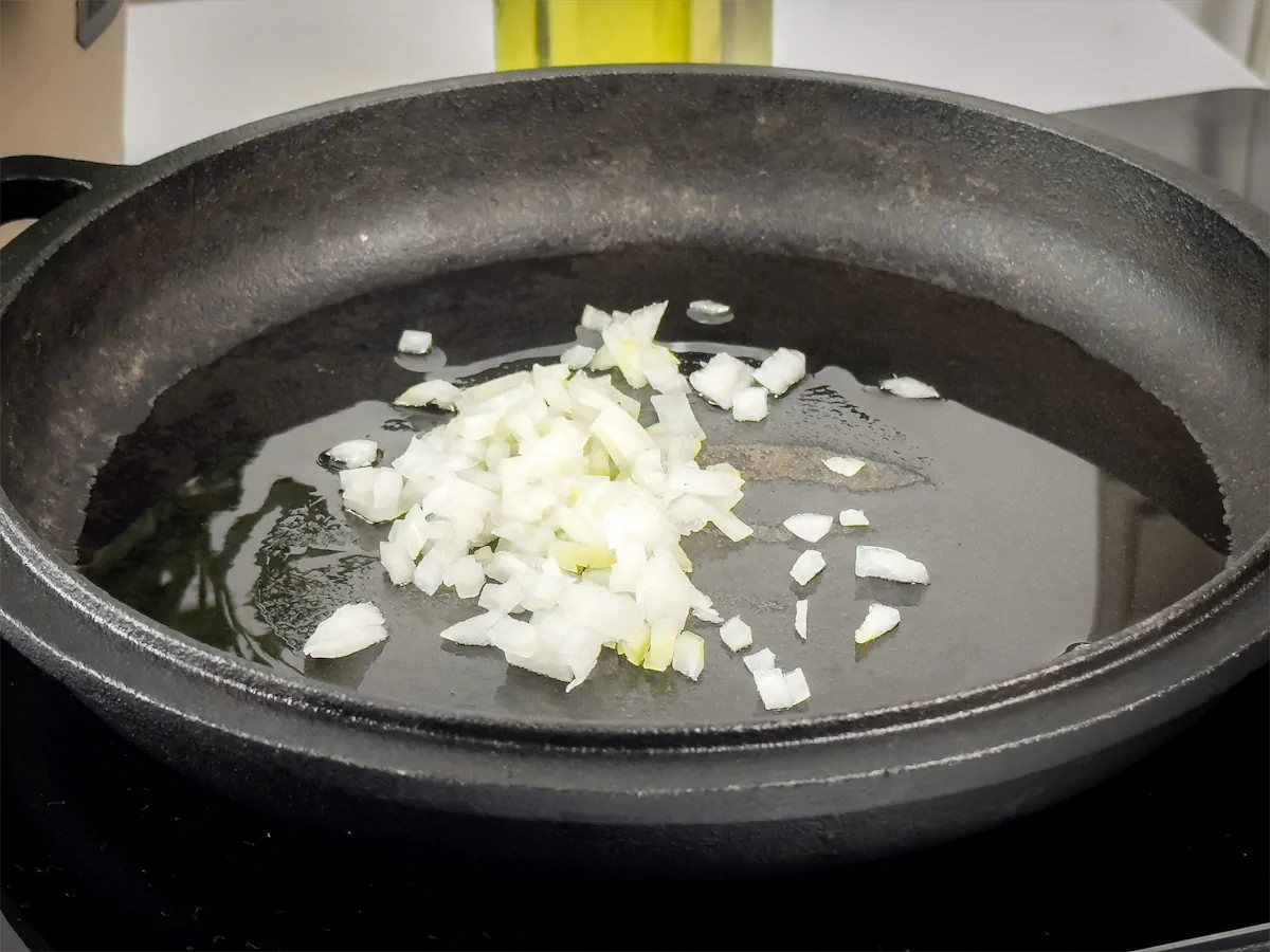 Chopped onions added to a cast iron skillet containing oil.