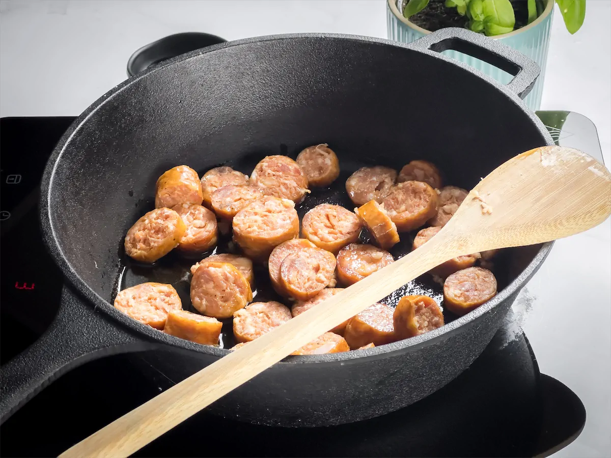Sautéing chopped sausages in a cast iron pan.
