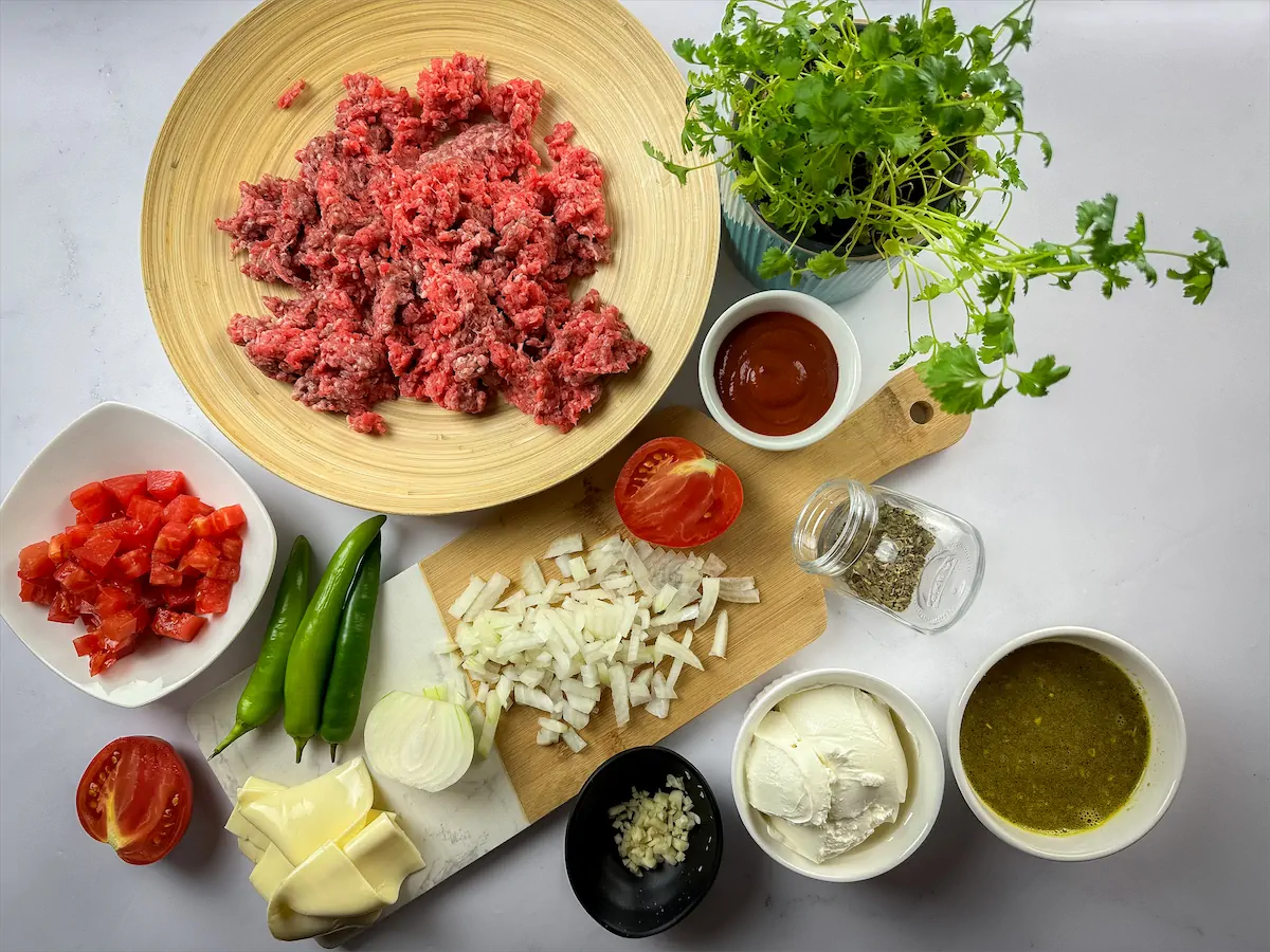 Ground beef, vegetable broth, diced tomatoes, cheeses, tomato sauce, and other ingredients arranged and displayed on the table.