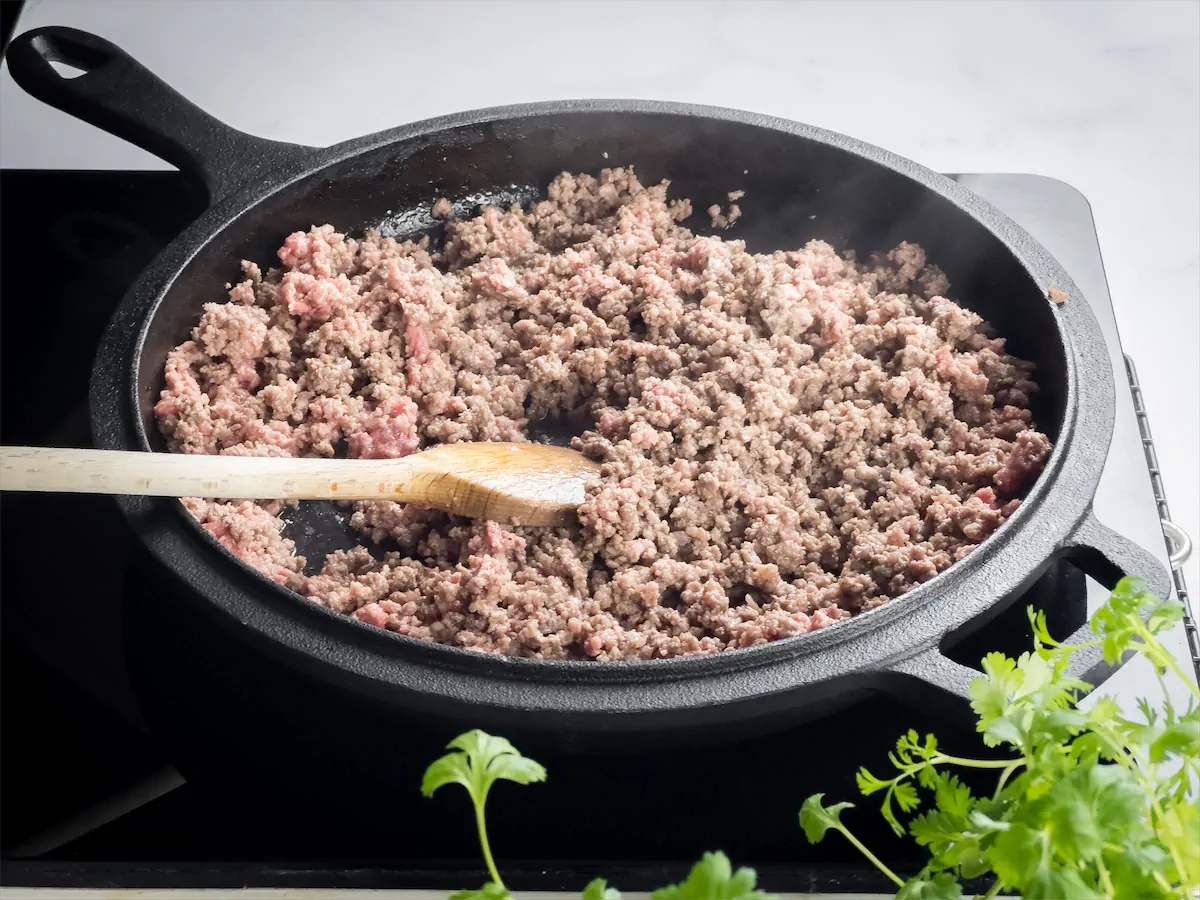 Browning the ground beef in a cast-iron skillet and stirring with a wooden spatula.