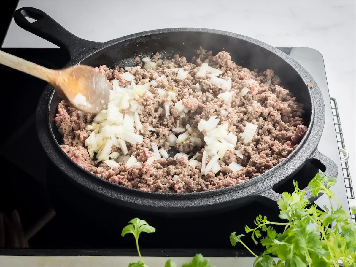 Diced onion added to beef cooking in the cast iron skillet.