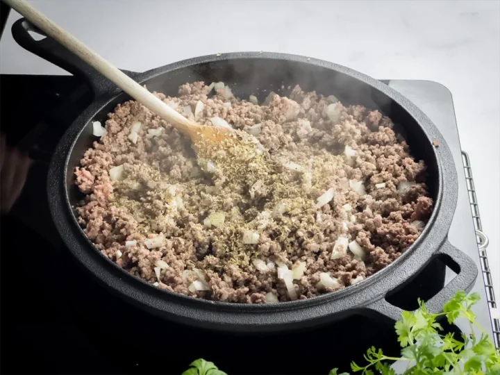Taco seasoning added to beef cooking in the cast iron skillet.