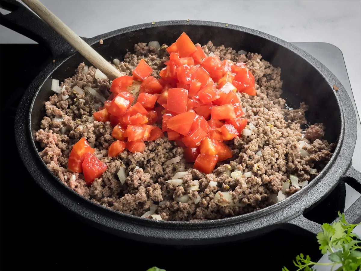 Diced tomatoes added to the beef cooking in cast iron skillet.