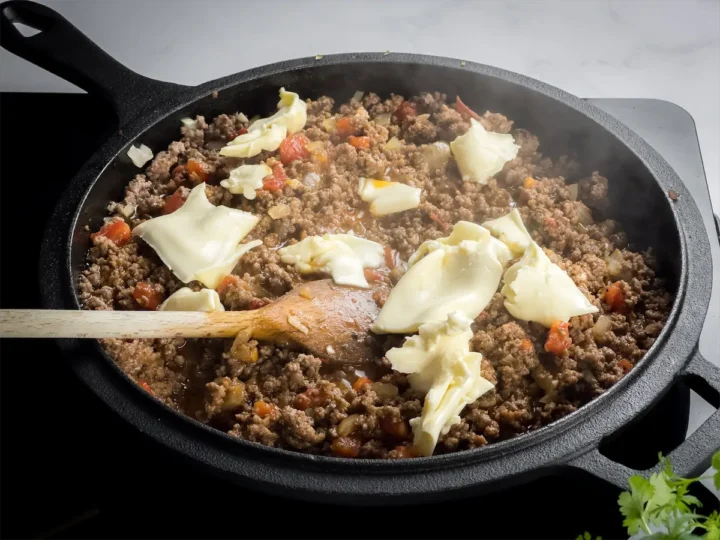 Gouda cheese is sprinkled into the meat sauce while preparing the keto taco casserole.