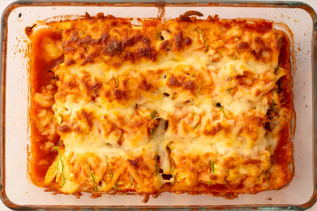 Baked cheesy keto zucchini enchiladas in a glass container ready to be served.