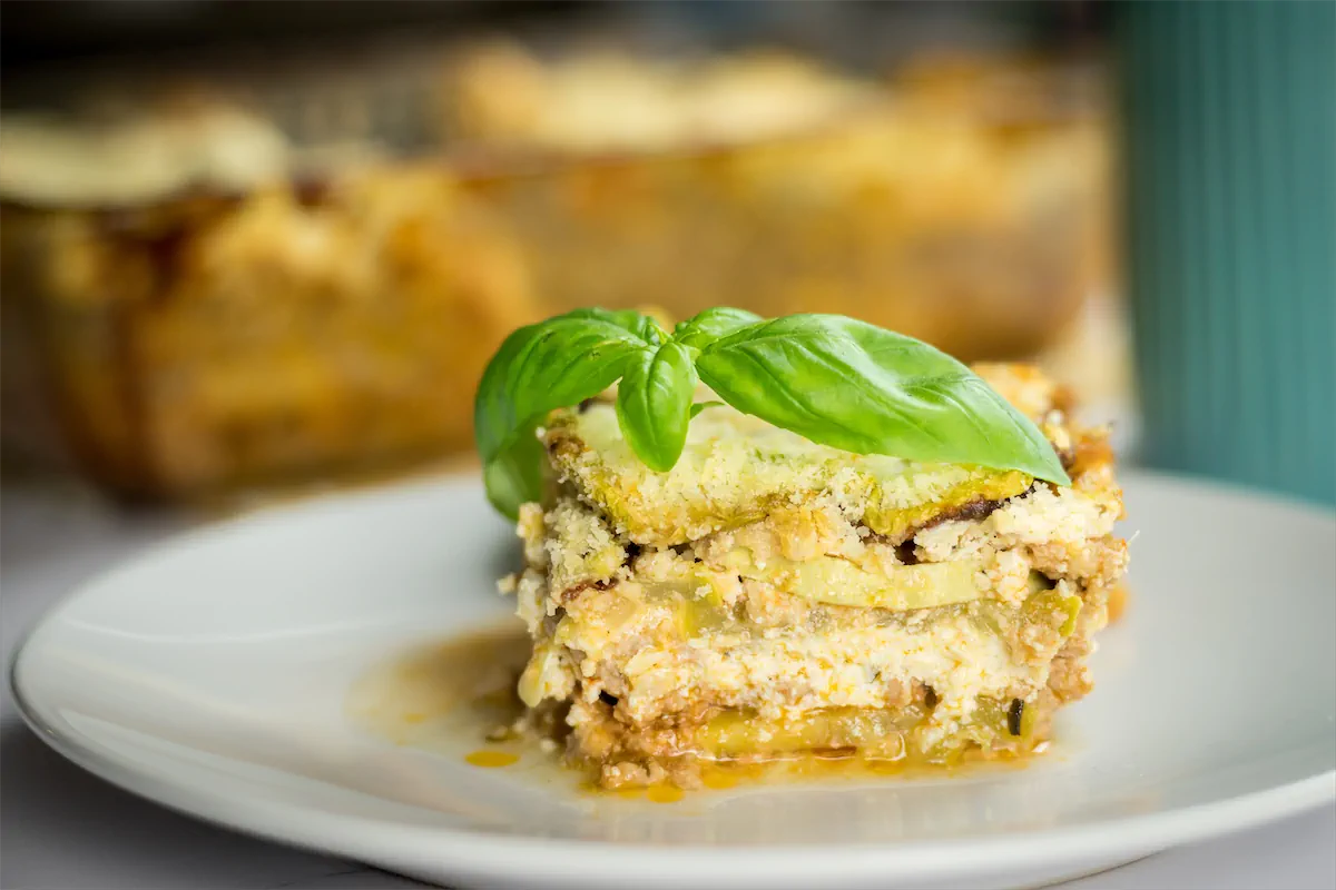 A portion of keto zucchini lasagna on a plate garnished with fresh basil leaves.