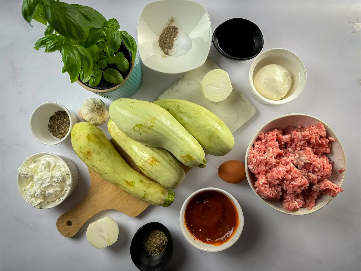 The necessary quantity of ground beef, marinara sauce, zucchini, cheeses, and other ingredients arranged and presented on the table.