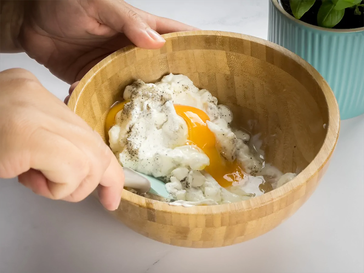 Mixing ricotta cheese, egg, salt, and pepper in a bowl.