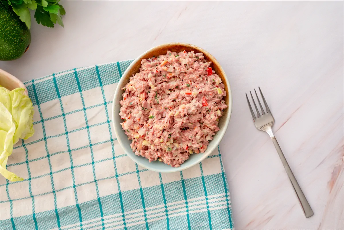 A bowl with a mixture of old-fashioned ham salad and a fork are on the table.