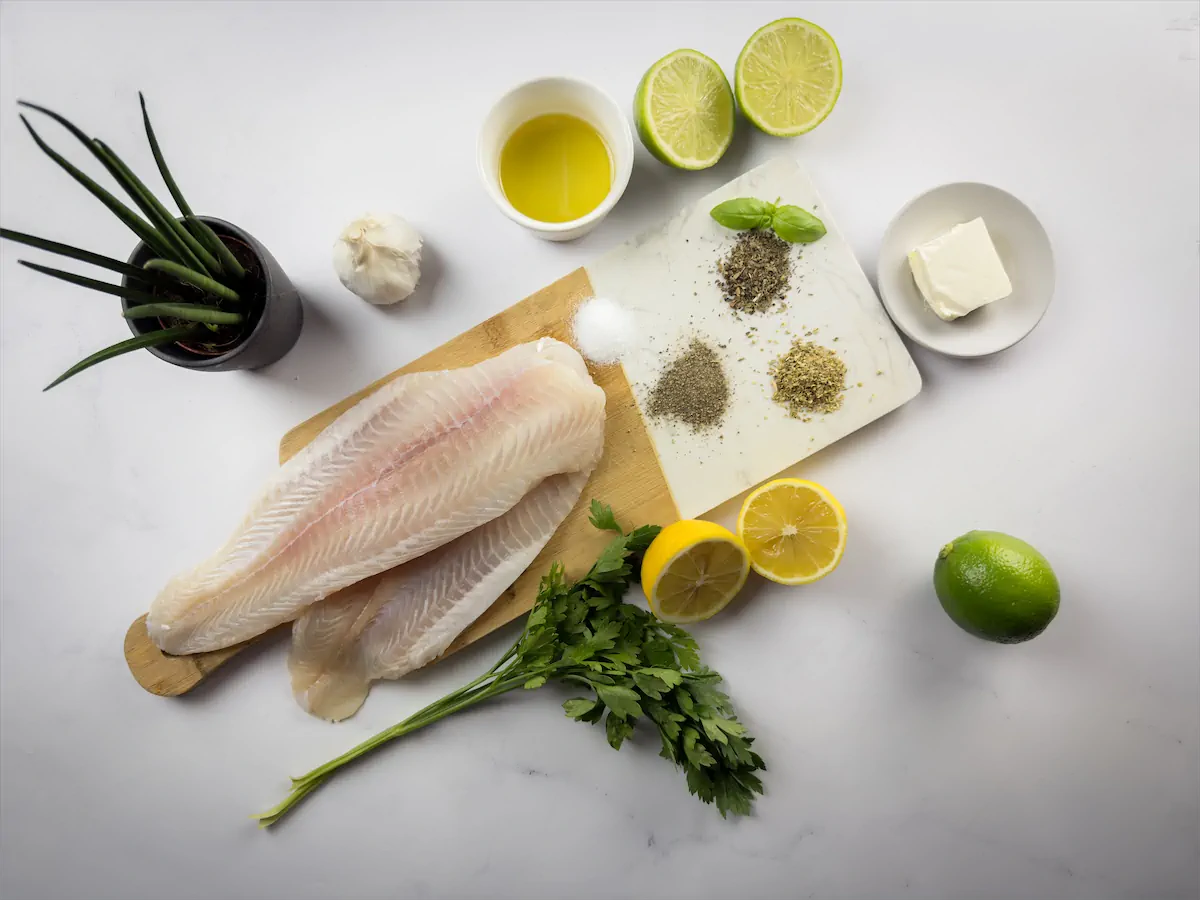 Halibut filets, lemon juice, butter, olive oil, minced garlic, and other spices are arranged and displayed on the table.