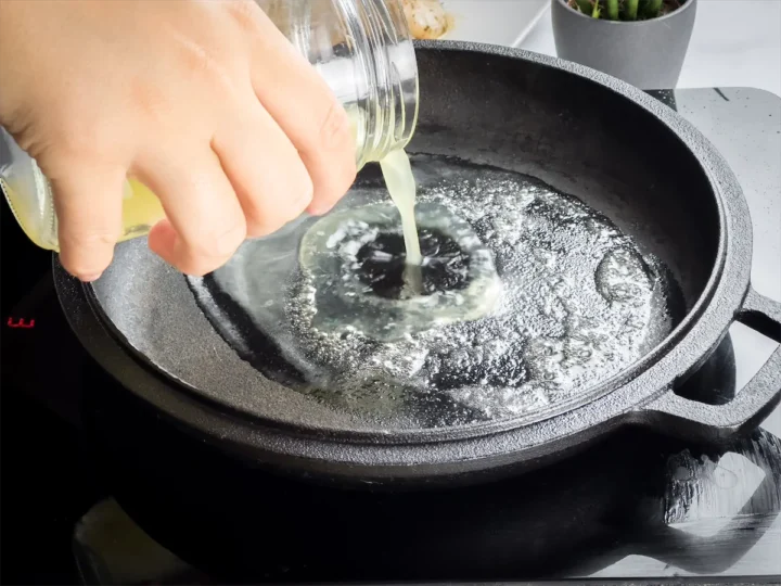 Pouring lemon juice into a cast iron skillet with melted butter.