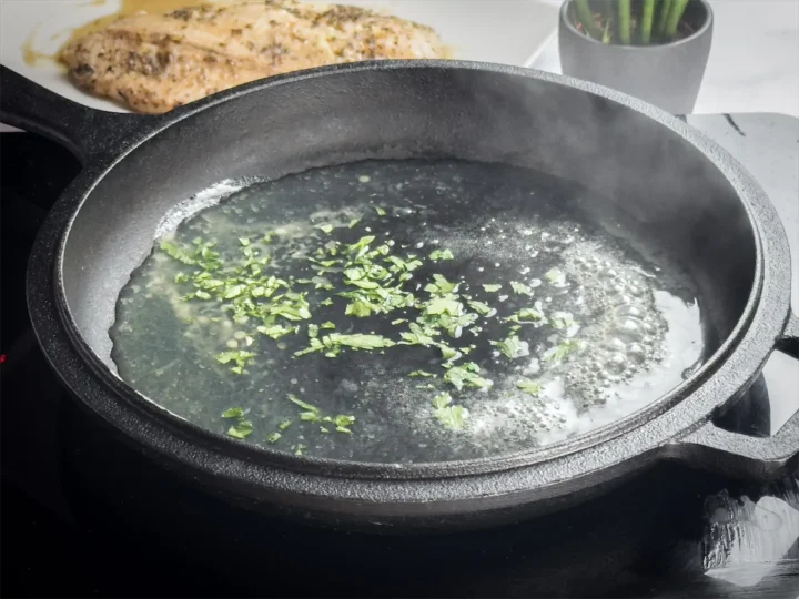 Lemon butter sauce with chopped parsley simmering in a cast iron skillet.