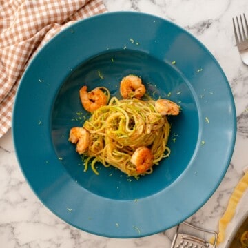 A plate of zucchini noodles with shirmp garnished with fresh green herbs is on the table.