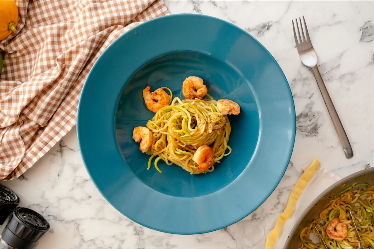 Zucchini noodles with shrimps served on a plate beside a fork on a table.