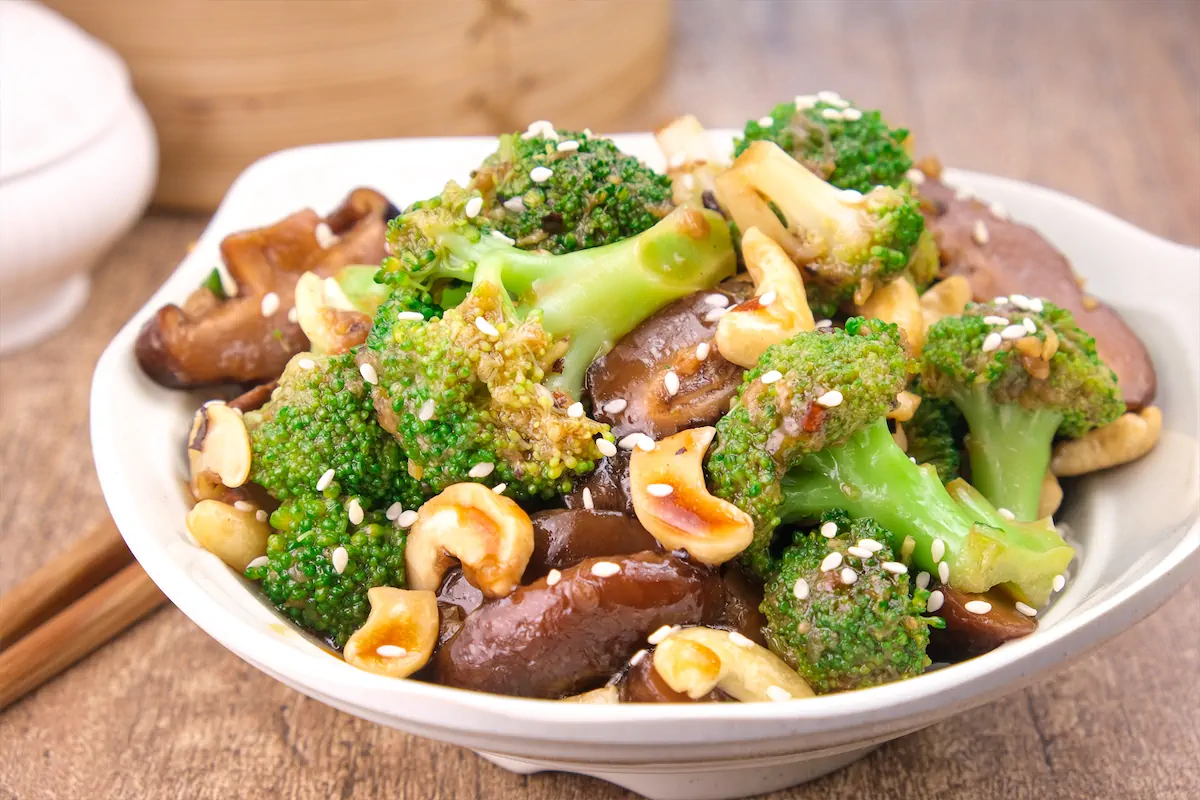 Home-made broccoli and mushrooms in an Asian sauce are presented in a bowl and topped with cashews.