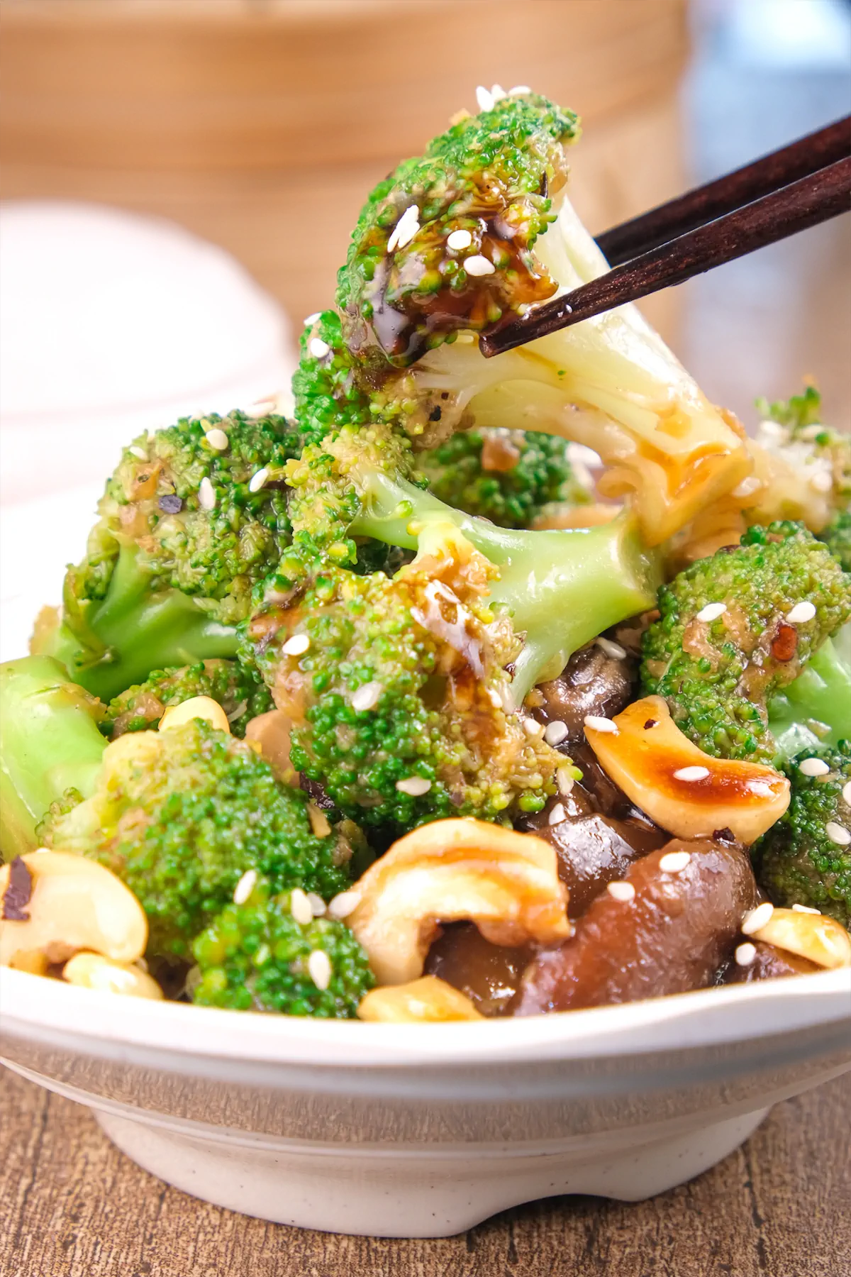 Homemade broccoli and mushrooms stir-fried in an Asian sauce, with a piece of broccoli being picked up using chopsticks.