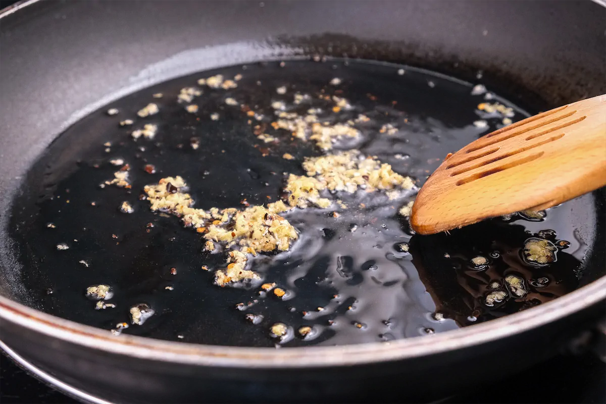 Cooking minced ginger in oil in a wok while stirring with a wooden spoon.