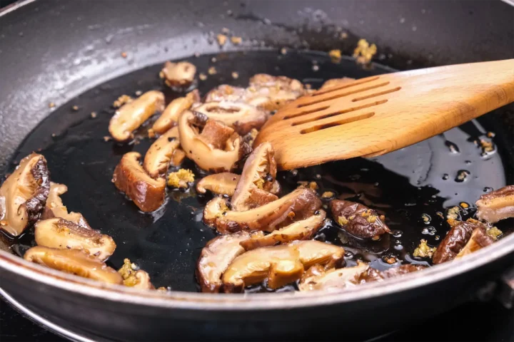 Cooking dehydrated mushrooms in a pan with minced garlic and stirring with a wooden spoon.