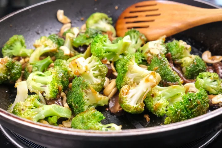 Stir-fried mushrooms and broccoli in an Asian sauce in a pan, ready to be served with a wooden spatula.