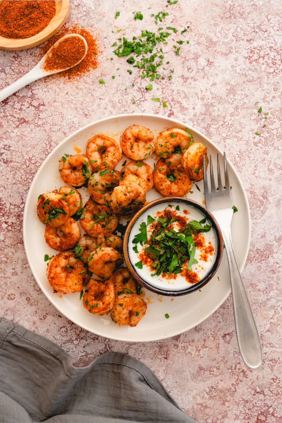 Keto Cajun shrimp on a white plate with a small bowl of dip and a fork.