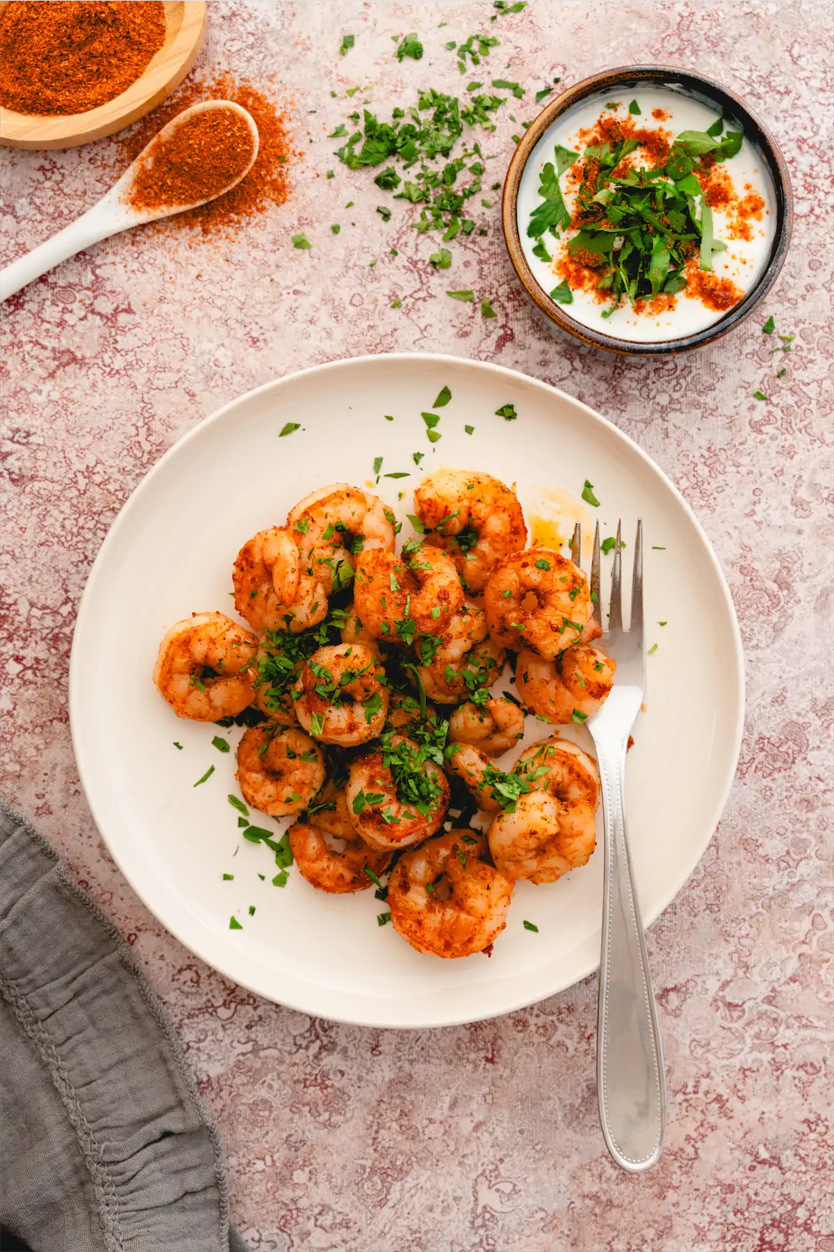 Low-carb Cajun shrimp served on a white plate with a side dip bowl and a fork.
