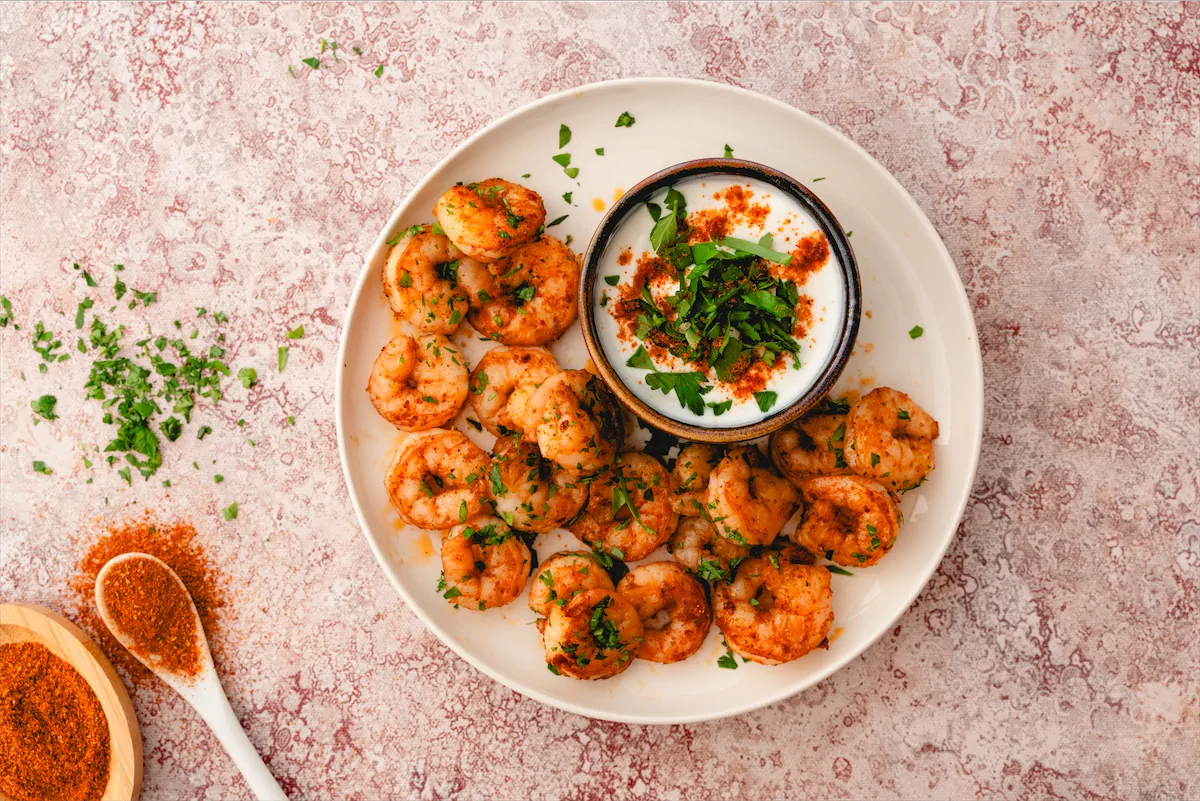 Serving of homemade keto Cajun shrimp on a white plate with dip and a fork.
