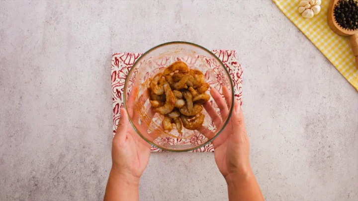 Two hands holding a transparent mixing bowl with the marinated shrimp.