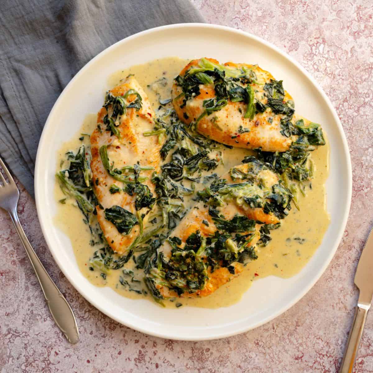 A plate featuring creamy Chicken Florentine beside a knife and fork.