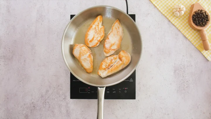 Chicken fillets flipped and sizzling to golden perfection in a stainless steel skillet.