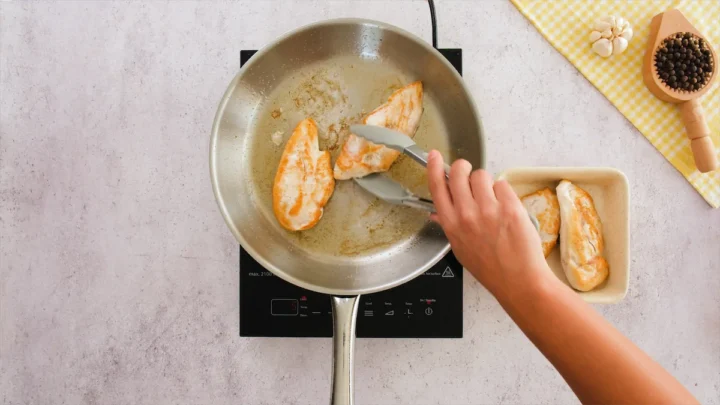 Transferring the cooked chicken from the skillet to a bowl with tongs.