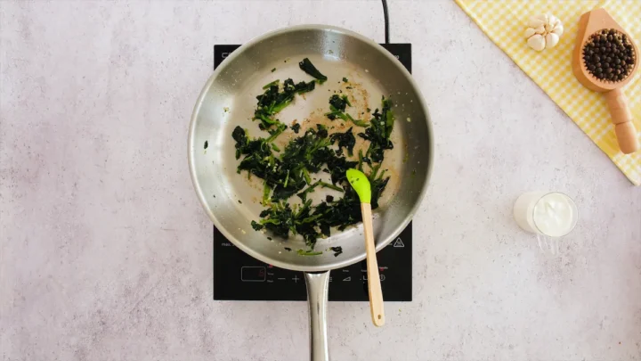 Sautéing the spinach with garlic in a stainless steel skillet.