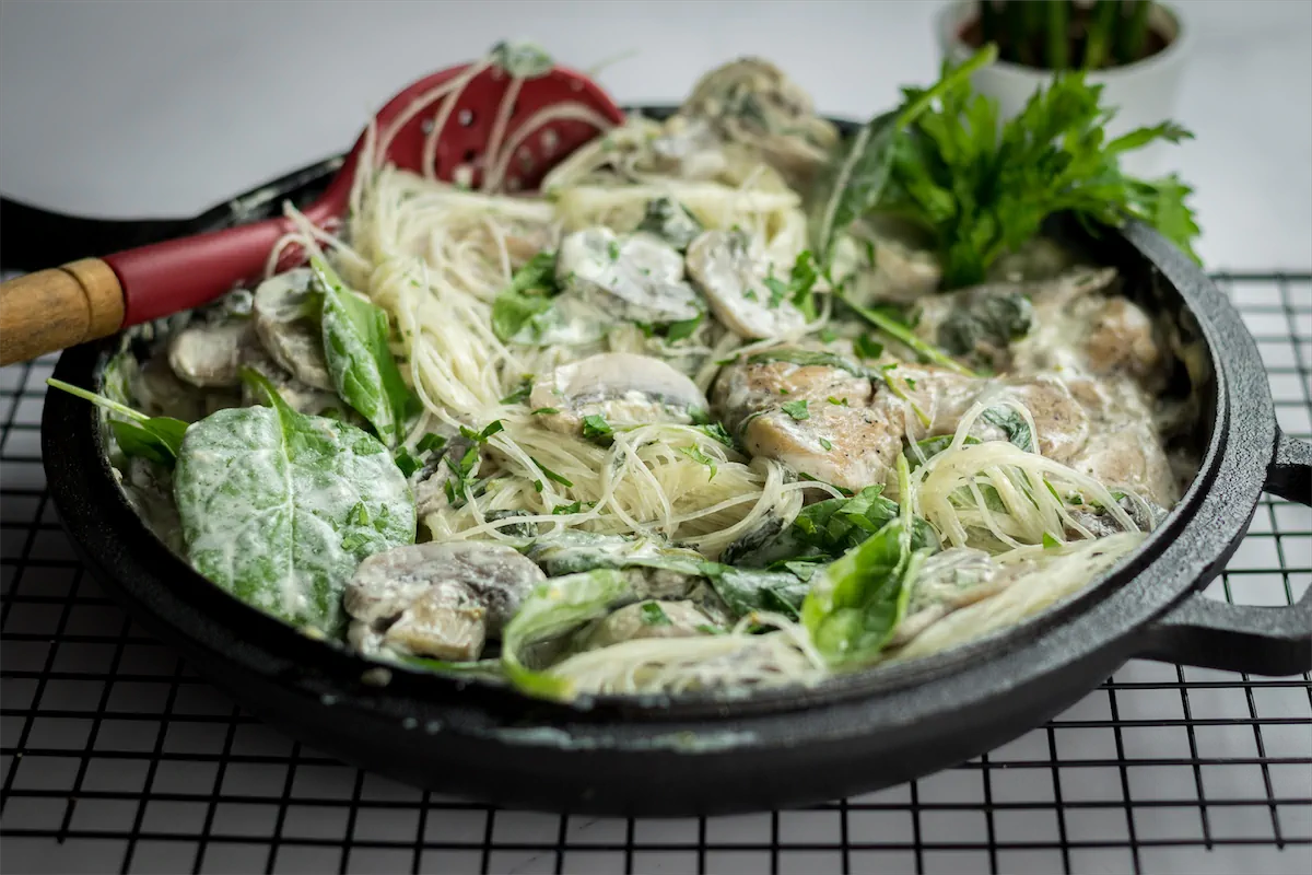 Keto creamy chicken mushroom dish in a cast iron skillet, prepared to be served with silicone spatula.