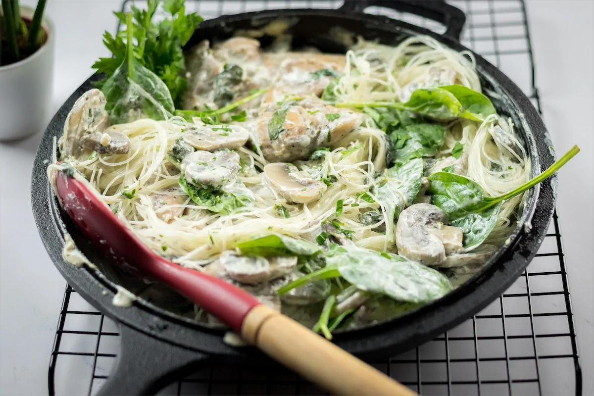 Homemade creamy chicken mushroom pasta in a cast iron skillet, ready for serving and accompanied by a silicone spatula.